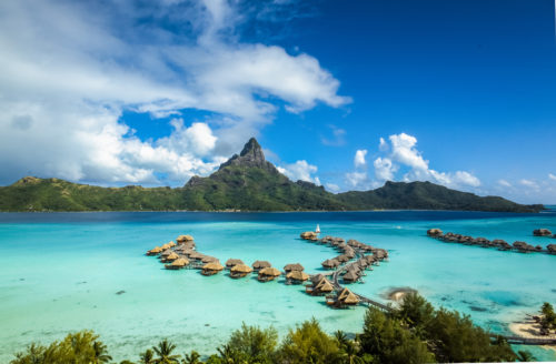 a group of huts in the water with Bora Bora in the background