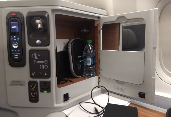 an airplane seat with a door open and a bottle of water