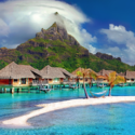 a beach with houses and a hammock on the water with Bora Bora in the background