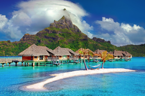 a beach with houses and a hammock on the water with Bora Bora in the background