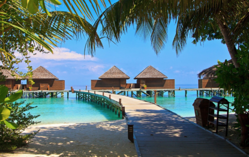 a walkway leading to a beach with huts on stilts