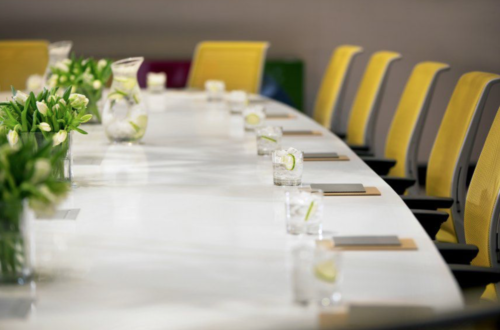 a long table with glasses of water and yellow chairs