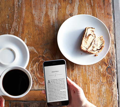 a hand holding a phone next to a plate of coffee and a piece of cake