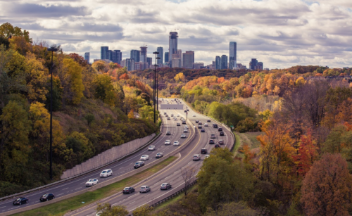 a highway with cars on it and trees with a city in the background