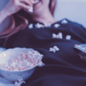 a woman lying down with popcorn in her mouth and a bowl of popcorn