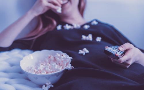 a woman lying down with popcorn in her mouth and a bowl of popcorn