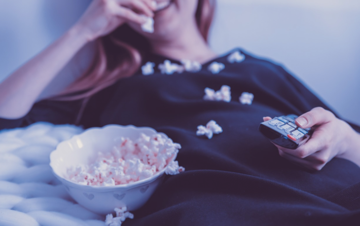 a woman lying in bed with popcorn and a bowl of popcorn