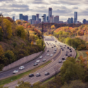 a highway with cars on it and trees with a city in the background