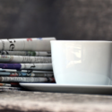 a cup and saucer next to newspapers