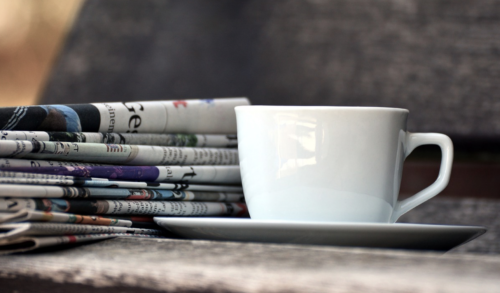 a cup and saucer next to newspapers