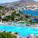 a pool with chairs and tables and chairs on a hill with water and hills in the background