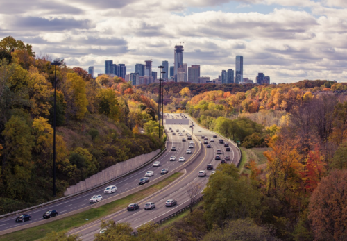 a highway with cars on it and trees with a city in the background