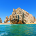 a large rock formation on a beach with Arch of Cabo San Lucas in the background