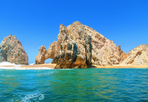 a large rock formation on a beach with Arch of Cabo San Lucas in the background