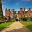 a large brick house with a driveway leading to it with Kentwell Hall in the background