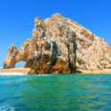 a large rock formation on a beach with Arch of Cabo San Lucas in the background