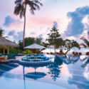 a pool with chairs and umbrellas and a beach in the background