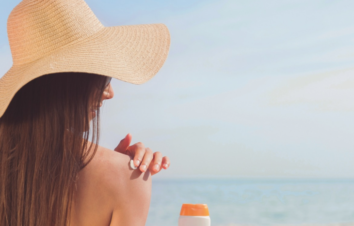 a woman wearing a hat and holding a sun cream