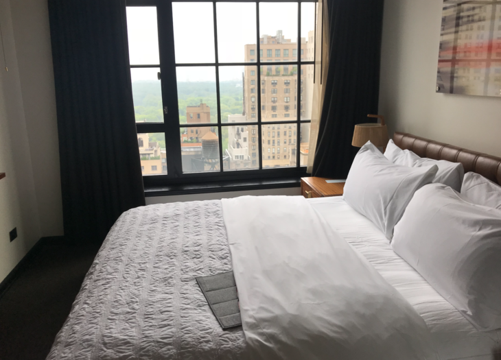 a bed with white sheets and pillows in a room with windows