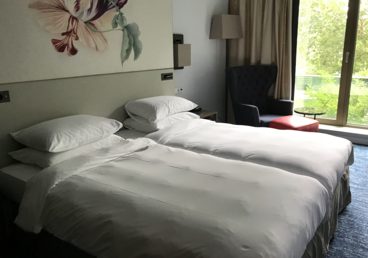 a bed with white sheets and pillows in a room with a flower painting