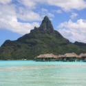 a group of huts on stilts in the water with Bora Bora in the background