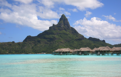 a group of huts on stilts in the water with Bora Bora in the background