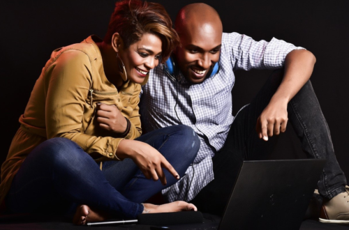 a man and woman sitting on the floor looking at a laptop