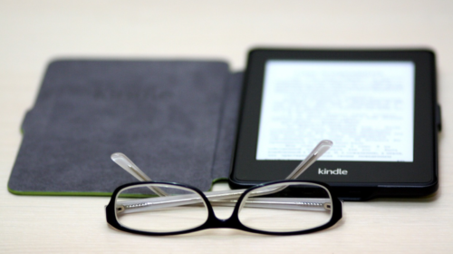 a pair of glasses next to a kindle