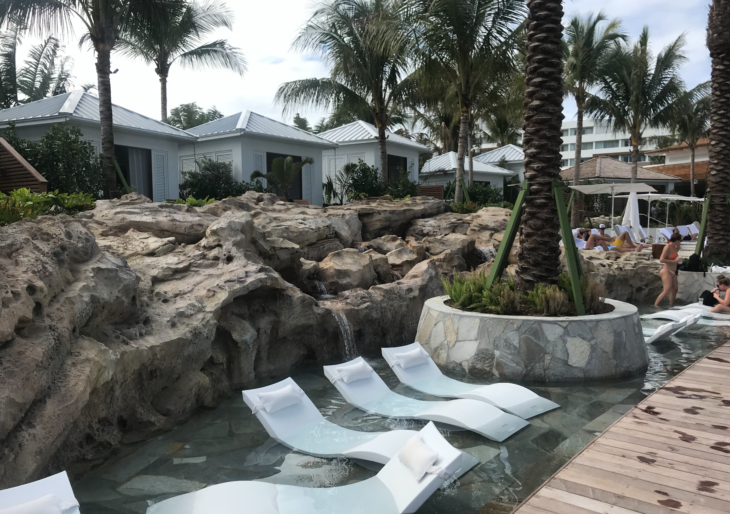 a pool with white chairs and rocks and palm trees