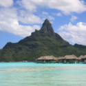 a group of huts on stilts in a body of water with Bora Bora in the background