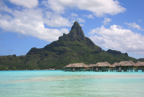 a group of huts on stilts in a body of water with Bora Bora in the background