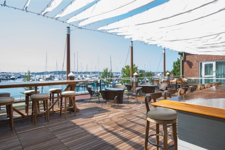 a patio with tables and chairs and a sailboat in the background