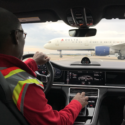 a man in a car with a yellow vest and a white airplane in the background