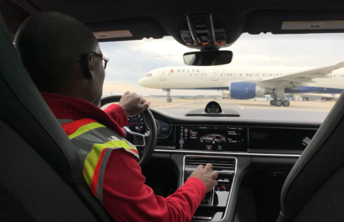 a man in a car with a yellow vest and a white airplane in the background