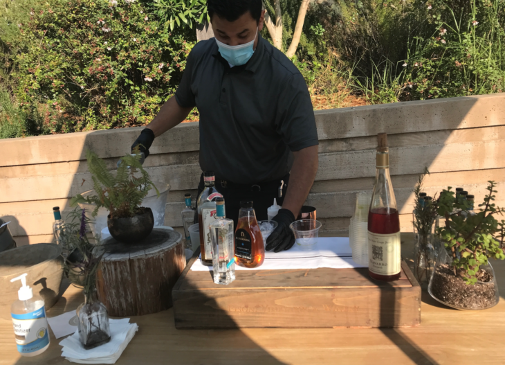 a man wearing a face mask and gloves standing at a table with bottles