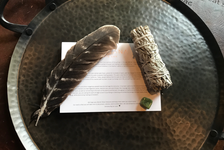 a feather and a white smudge stick on a black tray