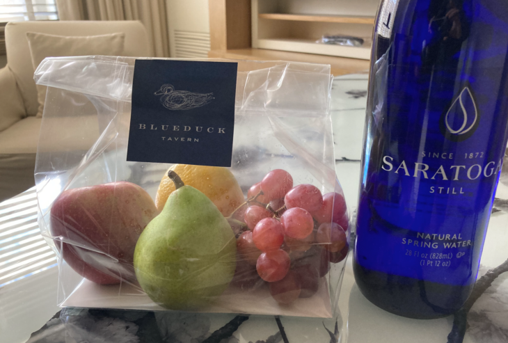 a plastic bag of fruit next to a bottle of wine