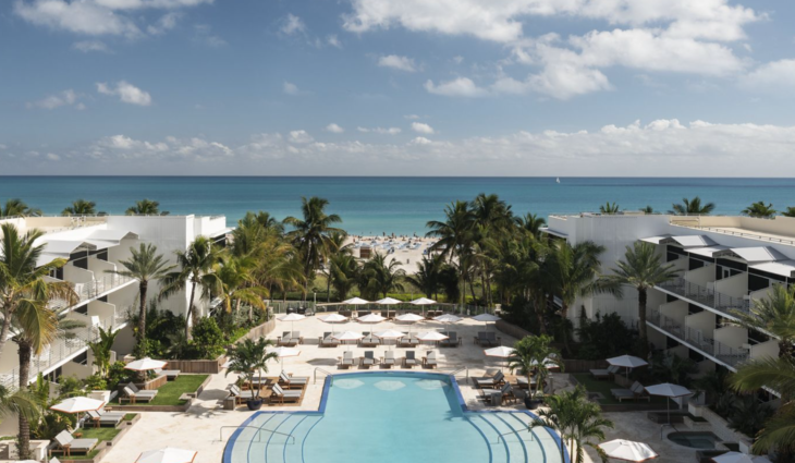 a swimming pool with chairs and palm trees in front of a beach