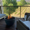 a fire pit on a deck with chairs and a vineyard